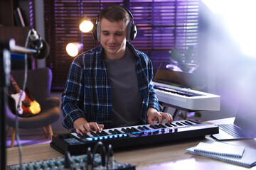 Man in headphones working with MIDI keyboard at table in home studio