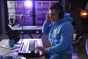 Man in headphones working with MIDI keyboard at table in home studio