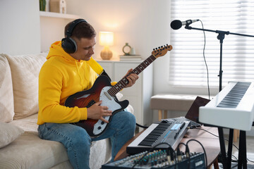 Man in headphones working with guitar and MIDI keyboard at table in home studio