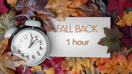 Autumn time change concept.  Fall Back 1 Hour message text with alarm clock surrounded by colorful...