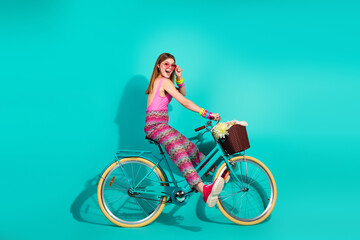 Vibrant young woman on a retro turquoise bicycle with flowers in a basket, posing against a stylish...