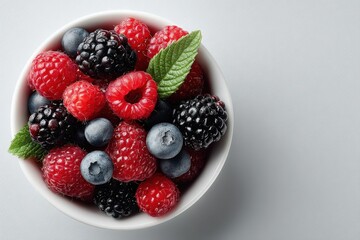 Flat lay style A bowl of mixed berries, including raspberries, blackberries, and blueberries, garnished with a mint leaf, set against a textured background.