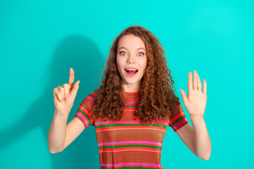 Excited red haired young woman makes playful hand gestures on turquiose background in casual...