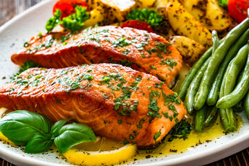 Seared salmon steaks with green string beans and roasted potatoes on wooden table