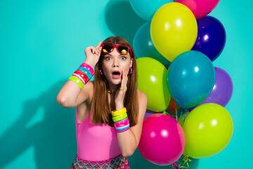 Young stylish woman in vibrant attire posing playfully with retro accessories and colorful balloons...