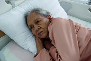 Senior female patient in pink gown resting on pillow with peaceful expression, symbolizing...