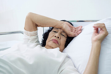 Female elderly patient in bed showing signs of fatigue, possibly reflecting chronic condition,...