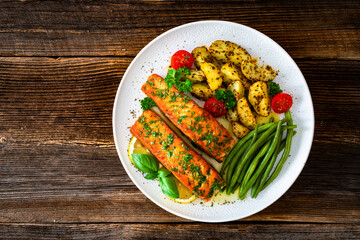 Seared salmon steaks with green string beans and roasted potatoes on wooden table