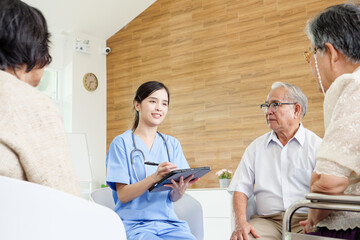 Professional Southeast Asian nurse consulting elderly patients in bright modern care facility, using laptop for health advice, symbolizing quality senior healthcare, trust, and compassion.