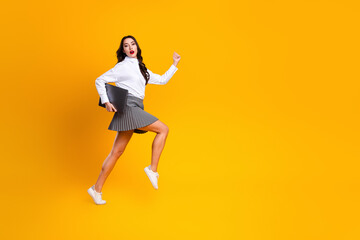 Fototapeta premium Confident young businesswoman holding laptop in dynamic pose against vibrant yellow background