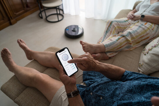 Senior man operating smart vacuum using smartphone app