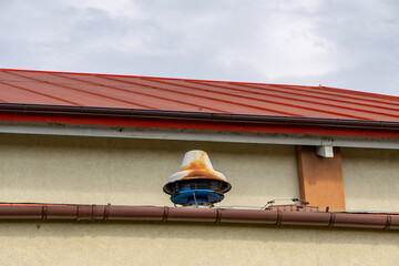 Old rusty civil defense alarm siren mounted on the wall under a red metal roof. Architectural...