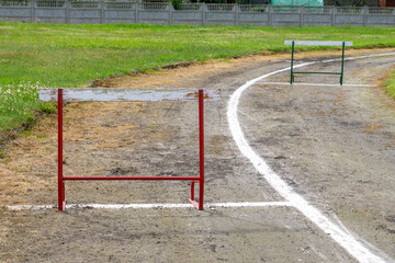 Improvised running track with hand-painted lines and training hurdles on a grassy field in an...