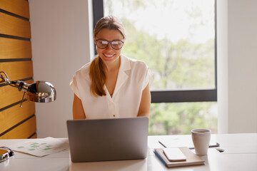 A young woman intensely focused on her laptop in a bright, stylish workspace that boasts a stunning...