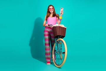 Fashionable young woman with phone and vintage bicycle on teal background showcasing trendy retro...