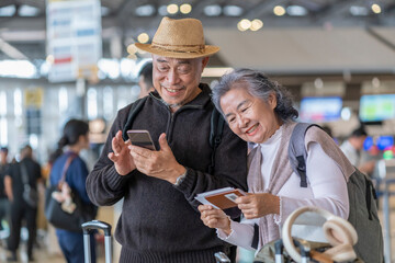 happy senior couple standing in the airport terminal,old woman holding passport and tickets,old man using smartphone online check in while waiting for boarding,elderly pensioner with modern lifestyle