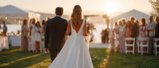 Couple walks down the aisle at sunset with father holding bride's hand during outdoor wedding ceremony