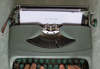 Hands typing the inspirational phrase live, love, laugh on a vintage typewriter, evoking nostalgia...