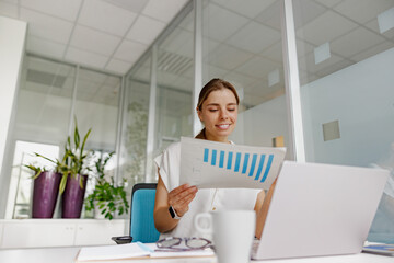 An accomplished businesswoman diligently reviews important data on paper while working in a stylish...