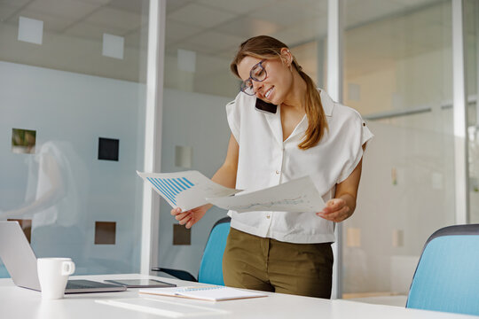 A dedicated professional woman is reviewing important paperwork while simultaneously multitasking on a phone call - Powered by Adobe