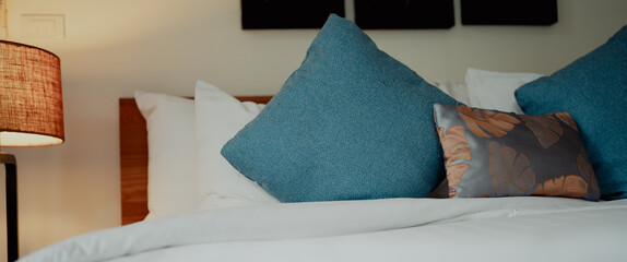Close-up of pillows arranged on a neatly made bed with wooden lamp and headboard. Soft textures and...
