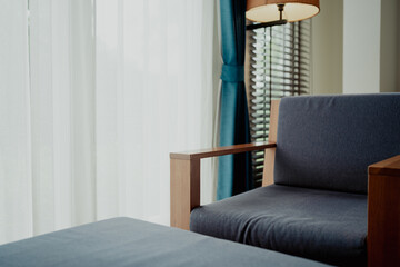 Wooden lounge chair by window with sheer curtain and warm lamp. Simple interior design evoking...