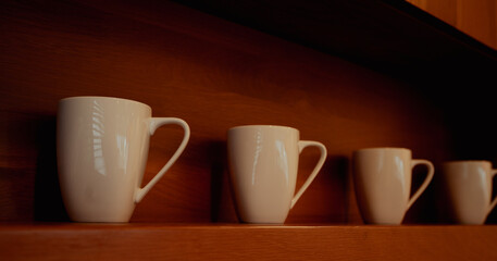 Minimal interior details with cozy lighting. Close-up of ceramic mugs on wooden shelf