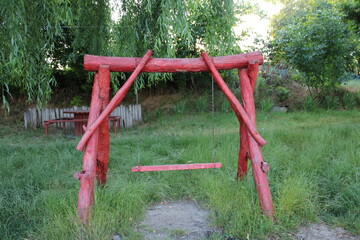 Red wooden swing set in a verdant garden.