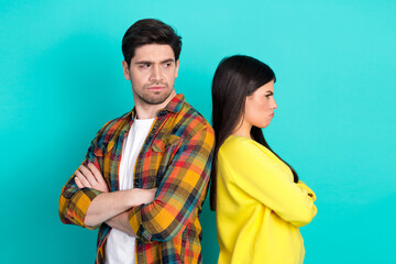 Young couple in disagreement posing with crossed arms against a teal background symbolizing...
