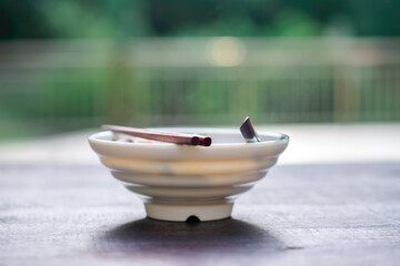 Traditional Asian ceramic bowl with chopsticks and tea served on a wooden surface outdoors with a...