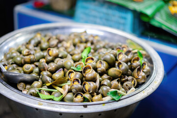 Close-up of a stainless steel bowl filled with cooked snails garnished with green herbs on a countertop in a casual dining setting
