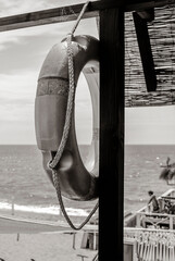 Close-up of a lifebuoy hanging on a wooden post at the beach with sea view in black and white. Vintage seaside atmosphere with safety concept and summer nostalgia. Framed composition and retro mood.