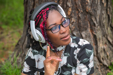 Happy African American Woman with Colorful Braids Listening to Music with Headphones in Park