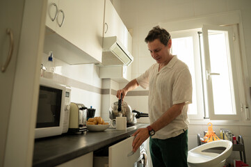Man preparing breakfast pouring hot water into cup in kitchen
