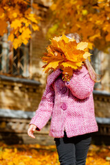 Little girl holding yellow autumn leaves, smiling outdoor park. Seasonal joy child happiness concept