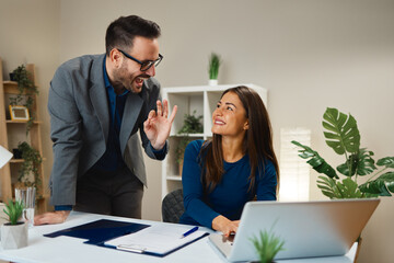Businessman gesturing ok sign to businesswoman working on laptop in office