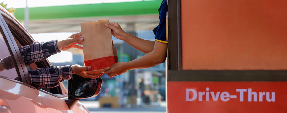 Hand Man in car receiving coffee in drive thru fast food restaurant. Staff serving takeaway order for driver in delivery window. Drive through and takeaway for buy fast food for protect covid19.