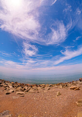 Dratamic coastal scene featuring a rocky beach under a vivid blue sky with wispy clouds. Fish eye...