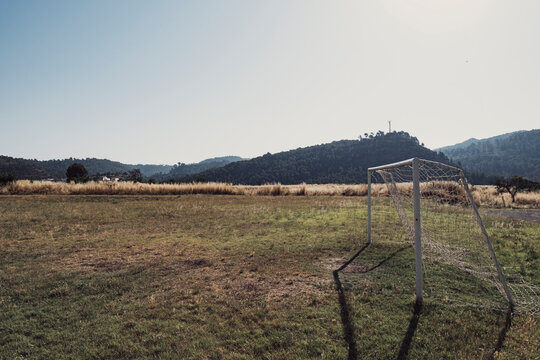 Rustic outdoor football field with metal goalposts on dry grass and dirt ground under clear sky, representing rural sports facilities, open landscapes and minimal urban development in countryside area