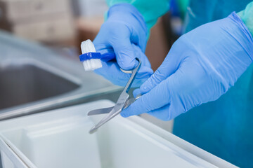 Close-up of professional hands in blue gloves using a small brush to clean medical scissors for...