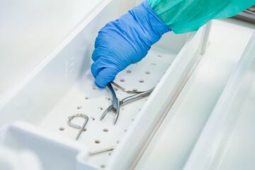 Close-up of a professional's gloved hand organizing sterile medical tools in a clean white tray,...