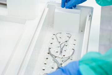 Close-up view of surgical instruments immersed in disinfectant liquid inside a medical tray,...