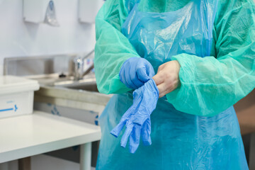 A healthcare professional's hands meticulously putting on blue disposable medical gloves,...