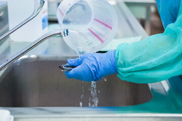 A professional wearing a protective gown and blue gloves cleans surgical tools with running water,...