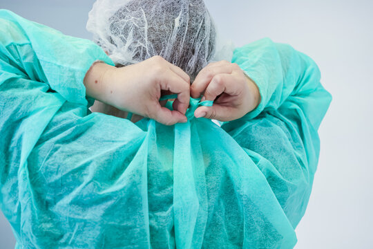 Rear view of a healthcare worker tying the back of a green disposable gown and hairnet, emphasizing the importance of sterile equipment in a professional setting