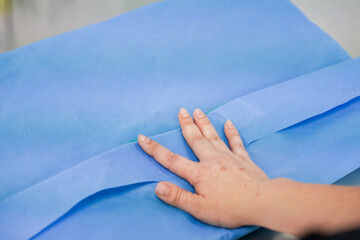 Close-up of a hand gently touching blue non-woven textile material, symbolizing hygienic...