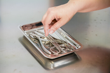 Close-up of a hand picking up sterile metallic instruments from a shiny medical tray, representing...