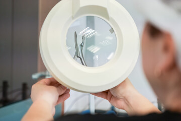A professional meticulously uses a large magnifying lamp with an integrated light to inspect a...