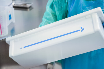 Close-up of a healthcare worker in sterile gloves holding a white plastic medical container with a...