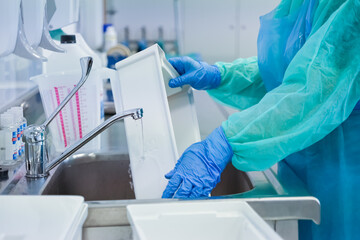 Close-up of a healthcare worker's gloved hands rinsing a white tray under a faucet, ensuring proper...